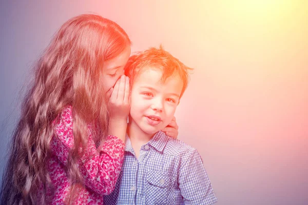 Girl in a red dress whispers in the ear a boy in a blue shirt in the sunlight