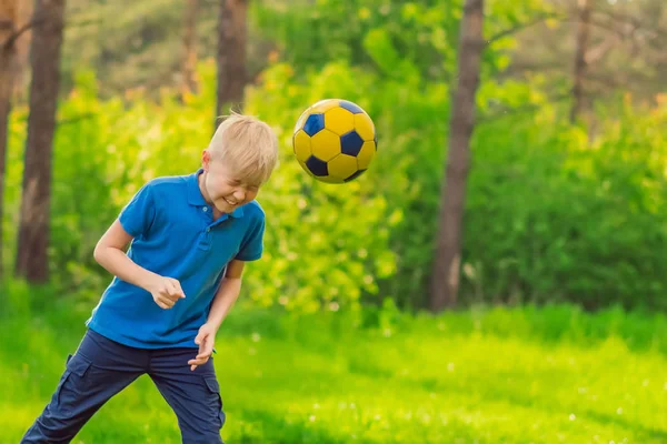 Blond boy in a blue T-shirt beats his head a soccer ball in the park