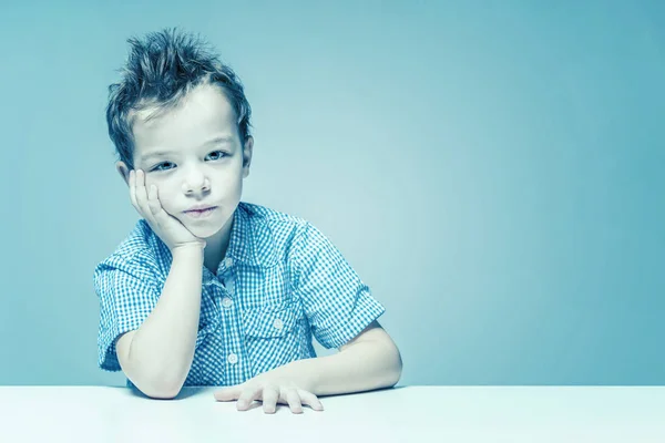 Cute thoughtful boy in a blue shirt at the table. Toned