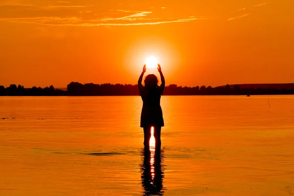 Woman is holding sun  in water at sunset