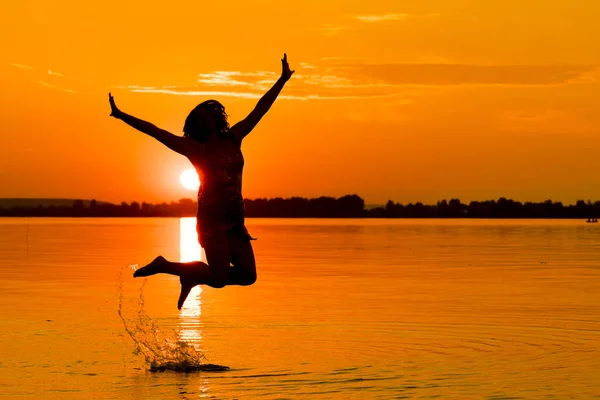 Silhouette of a woman jumping in the water at sunset