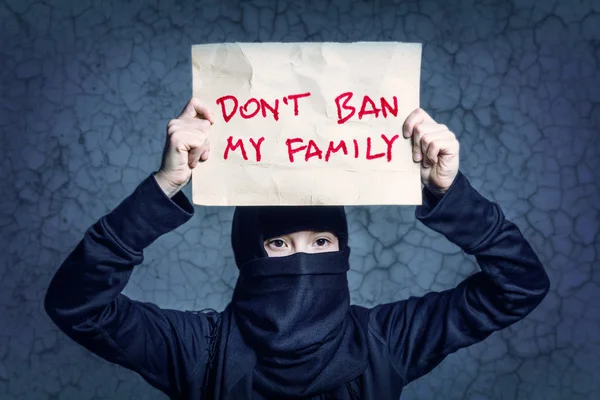 碑文とポスターを持って黒のヒジャーブのイスラム教徒の少女はありません禁止私の家族で壁に亀裂します — ストック写真