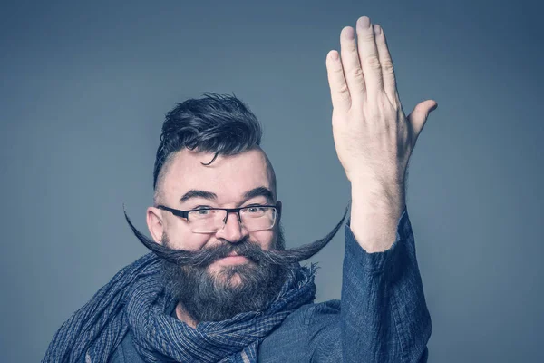 戴着长胡子的眼镜的成年大胡子男子举起他的手在灰色的背景 — 图库照片