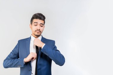 Mavi elbiseli Genç çekici adam kravat gri bir arka plan üzerinde düzeltir. İzole