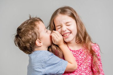 Mavi gömlekli çocuk gri bir arka plan üzerinde kırmızı elbiseli bir kız kulağına fısıldar. İzole