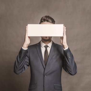 Gri bir arka plan üzerinde beyaz bir işaret tutan mavi elbiseli Genç çekici adam