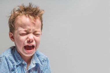 Gri bir arka plan üzerinde küçük çocuk ağlıyor 