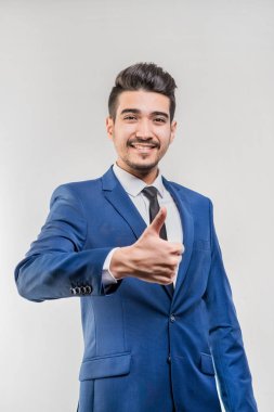 Gri bir arka plan üzerinde başparmak gösterilmesini mavi elbiseli Genç çekici adam. İzole