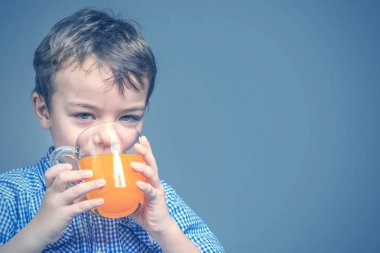 Mavi gömlekli şirin küçük çocuk içecekler portakal suyu mavi bir arka plan üzerinde