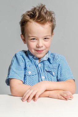 Sevimli çocuk gri bir arka plan üzerinde masada oturan mavi gömlekli. İzole