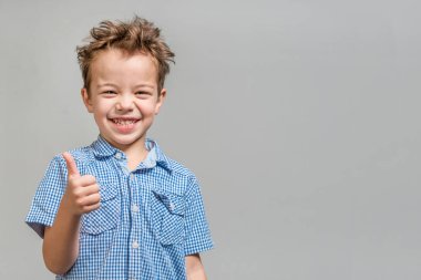 Mavi gömlekli başparmak gri bir arka plan üzerinde gösterilen boy gülümseyerek. İzole