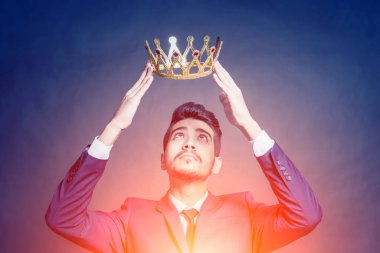 Parlak parlayan altın bir taç başını tutan mavi elbiseli Genç çekici adam