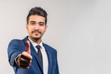 Gri bir arka plan üzerinde başparmak gösterilmesini mavi elbiseli Genç çekici adam. İzole