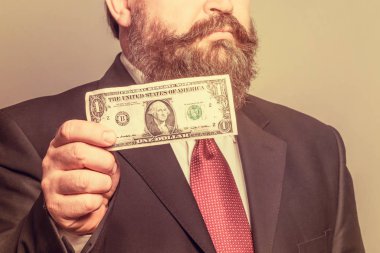 Bir dolar tutan elbiseli yetişkin sakallı adam. Tonda