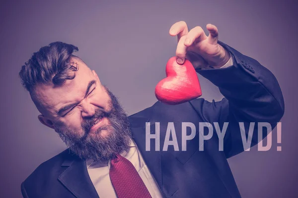 Brodaty Mężczyzna Garniturze Obrzydzeniem Trzymając Czerwone Serce Napisem Happy Stonowanych — Zdjęcie stockowe