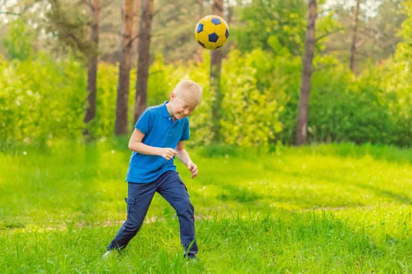 Blond boy in a blue T-shirt beats his head a soccer ball in the park