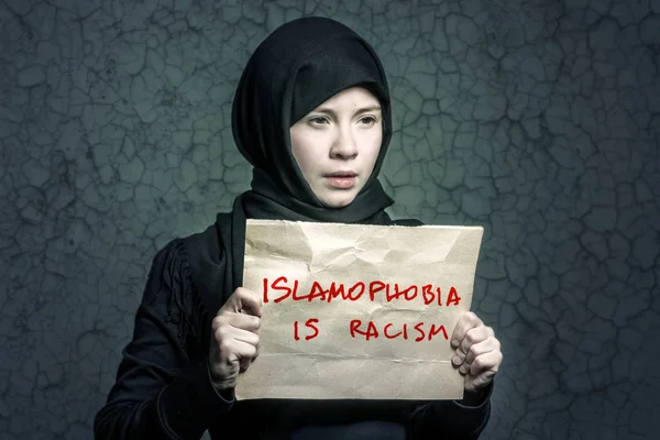碑文とポスターを持って黒のヒジャーブのイスラム教徒の少女恐怖症は人種差別と背景の壁に亀裂します — ストック写真