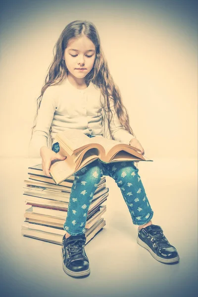 Cute girl with a book sitting on a pile of books. Toned