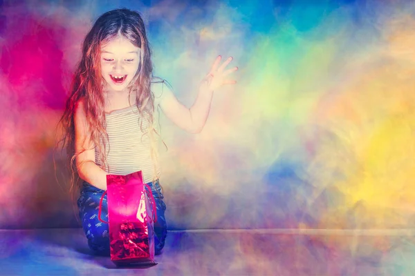 Mädchen Sieht Einer Rot Leuchtenden Geschenktüte Auf Buntem Hintergrund Aus — Stockfoto