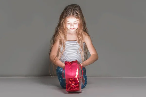 Chica Mira Una Bolsa Regalo Brillante Rojo Sobre Fondo Gris —  Fotos de Stock