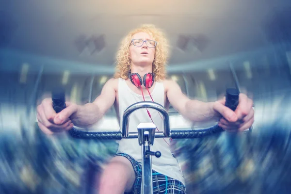 Thin curly blond guy with glasses on a stationary bike
