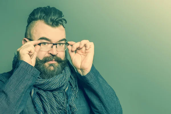 Adult bearded man in a scarf correcting glasses on a green background. Toned