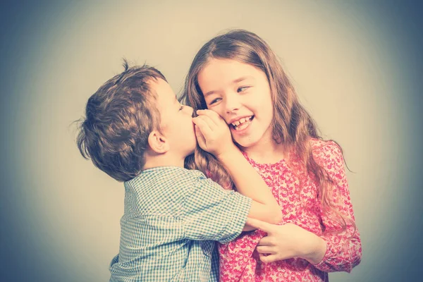 Boy in a blue shirt whispers in the ear a girl in a red dress. Toned