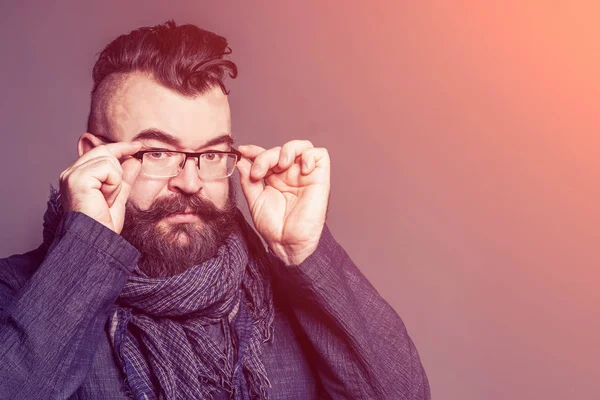 Adult bearded man in a scarf correcting glasses in the sunlight. Toned