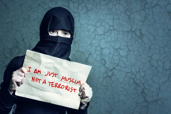 身穿黑色头巾的穆斯林女孩拿着一张写着 我只是穆斯林不是穆斯林不是恐怖分子 的海报 背景墙上有裂缝 — 图库照片
