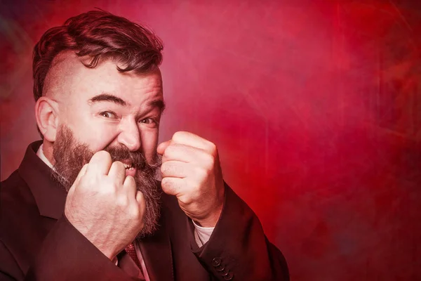 赤い背景の上の拳を示すスーツで積極的な大人の髭の男 — ストック写真