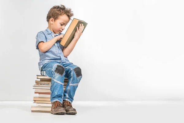 Cute boy with a book sitting on a pile of books on a white background