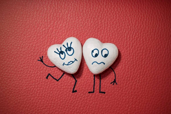 Two white hearts with happy and sad faces on red leather background