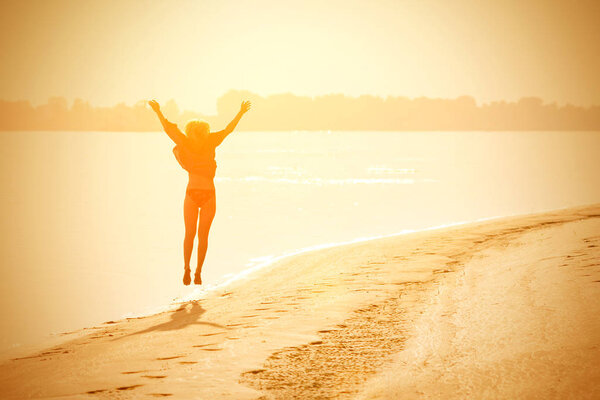 Blond girl teenager jumping up on the beach in the sunshine