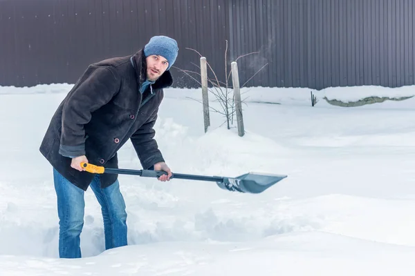 Man in winter clothes cleans snow shovel on courtyard. Toned