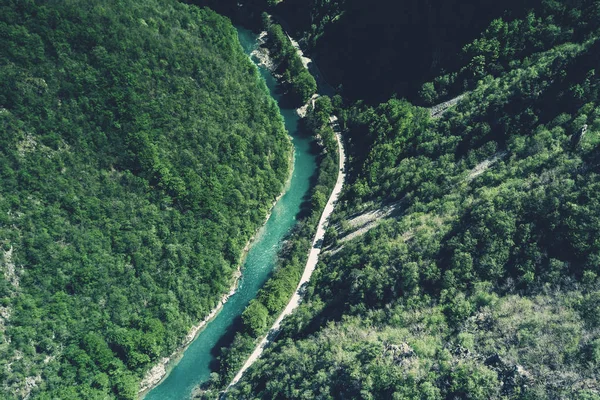 Top view of the river and asphalt road in the mountains surrounded by a green forest