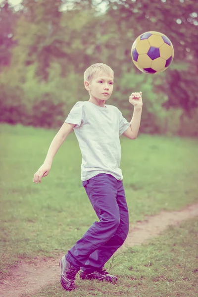 Blond boy in a white T-shirt kicks a soccer ball in the park. Toned