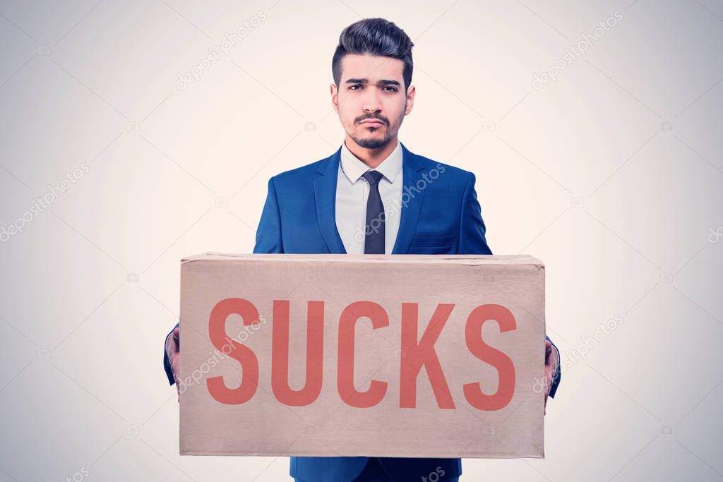 Attractive young man in a blue suit holding a cardboard box with the red inscription SUCKS in his hands