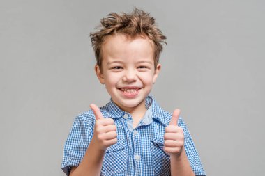 Mavi gömlekli başparmak gri bir arka plan üzerinde gösterilen boy gülümseyerek. İzole