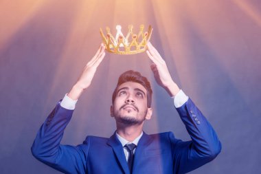 Parlak parlayan altın bir taç başını tutan mavi elbiseli Genç çekici adam