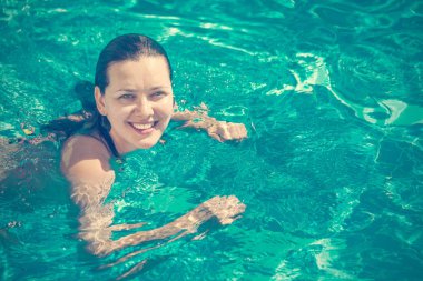 Yüzme havuzunda bir gülümsemeyle bikinili güzel bir esmer kadın