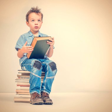 Sevimli çocuk mavi gömlekli bir yığın kitap bej renkli bir arka plan üzerine bir kitap üzerinde oturuyor. Tonda