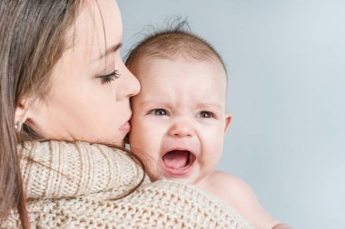 Gri bir arka plan üzerinde bir bebek tutan genç kadın