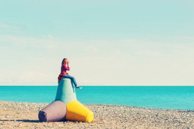 Sahilde bir beton tetrapod üzerinde oturan kadın