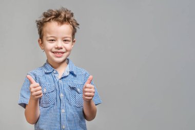 Mavi gömlekli başparmak gri bir arka plan üzerinde gösterilen boy gülümseyerek. İzole