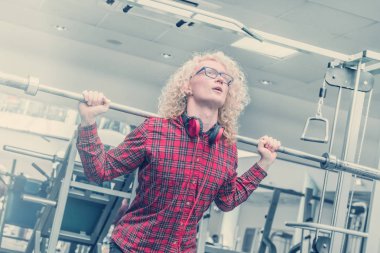 Genç sarışın adam kırmızı gömlekli ve spor salonunda bir halter kaldırma kulaklıklar ile.
