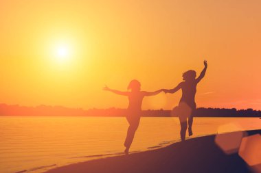 Gün batımında sahilde çalıştıran elele bir kadın silüeti