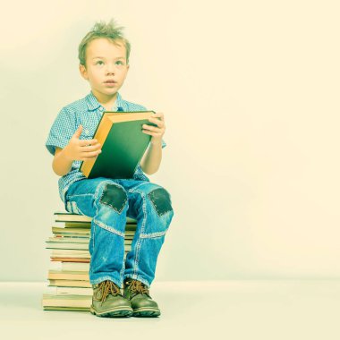 Sevimli çocuk mavi gömlekli bir yığın kitap üzerinde oturan ve bir kitap. Tonda