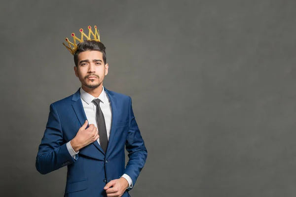 灰色の背景に彼の頭には王冠と紺のスーツの若い魅力的な男 — ストック写真