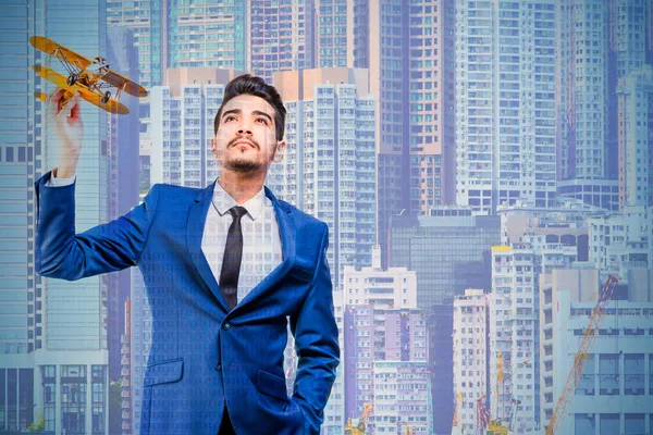 Young attractive man in a blue suit holding a yellow airplane model on the background of skyscrapers