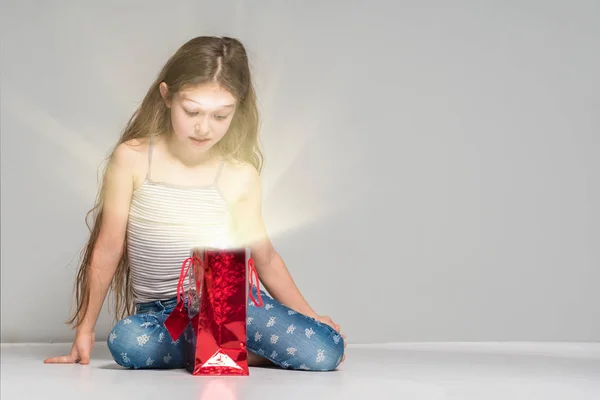 女の子は 灰色の背景に赤の光るギフト バッグ — ストック写真